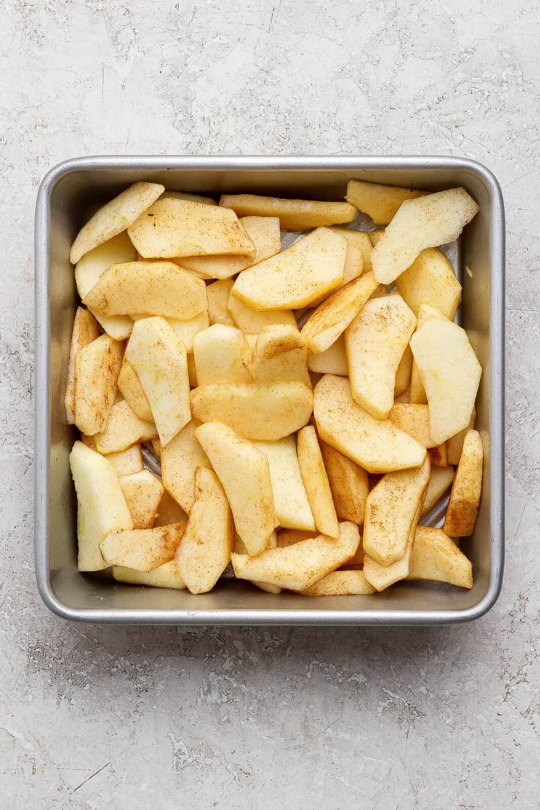 Slices of apple tossed in ground cinnamon and placed in a baking pan for healthier apple crisp.