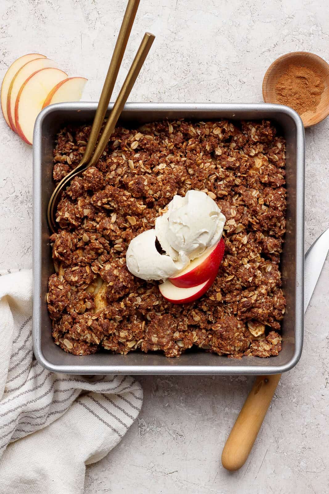 Fully baked healthy apple crisp in a pan with ice cream and apple slices on top.