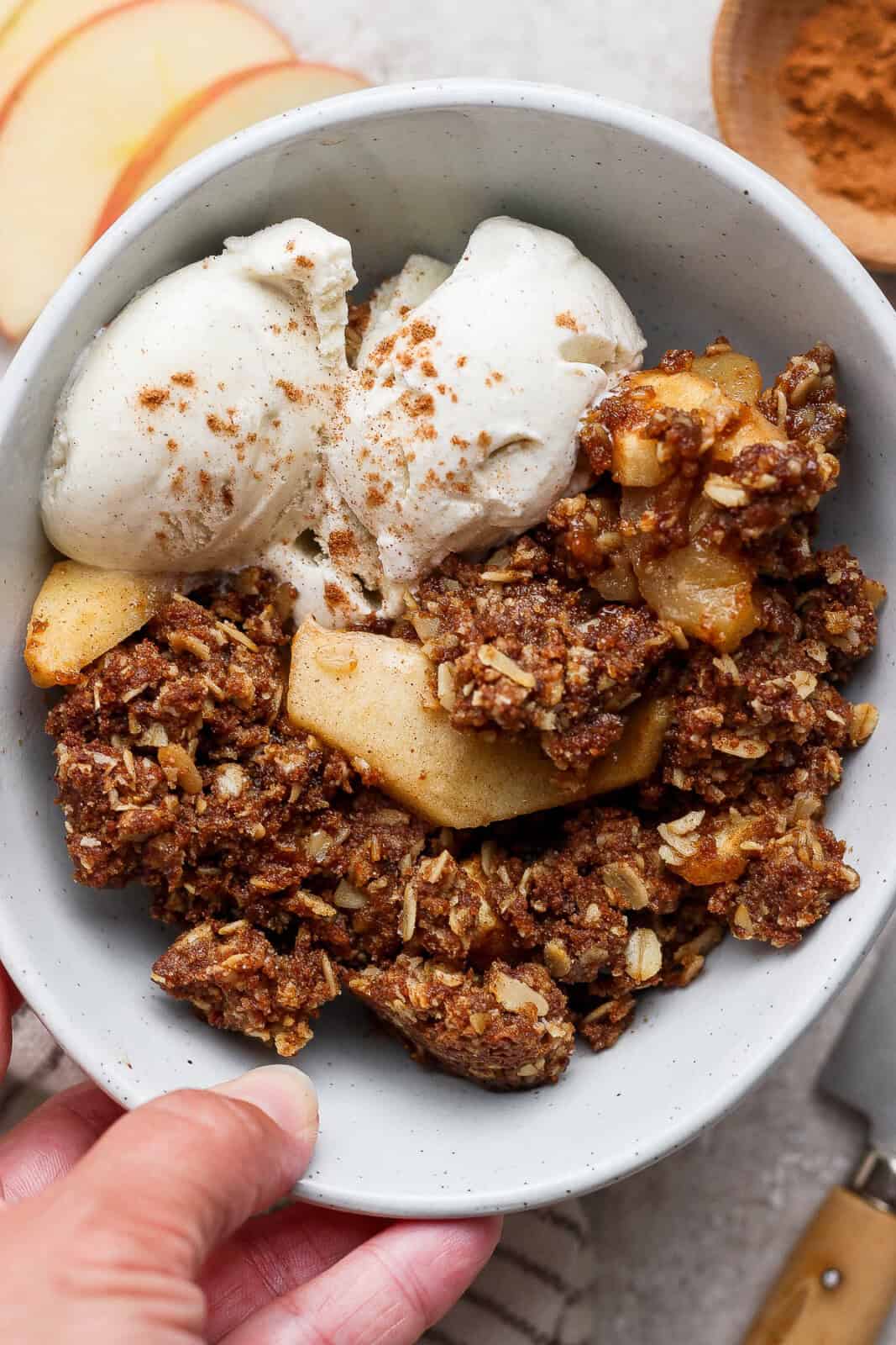 A serving of healthy apple crisp in a bowl with two scoops of vanilla ice cream.