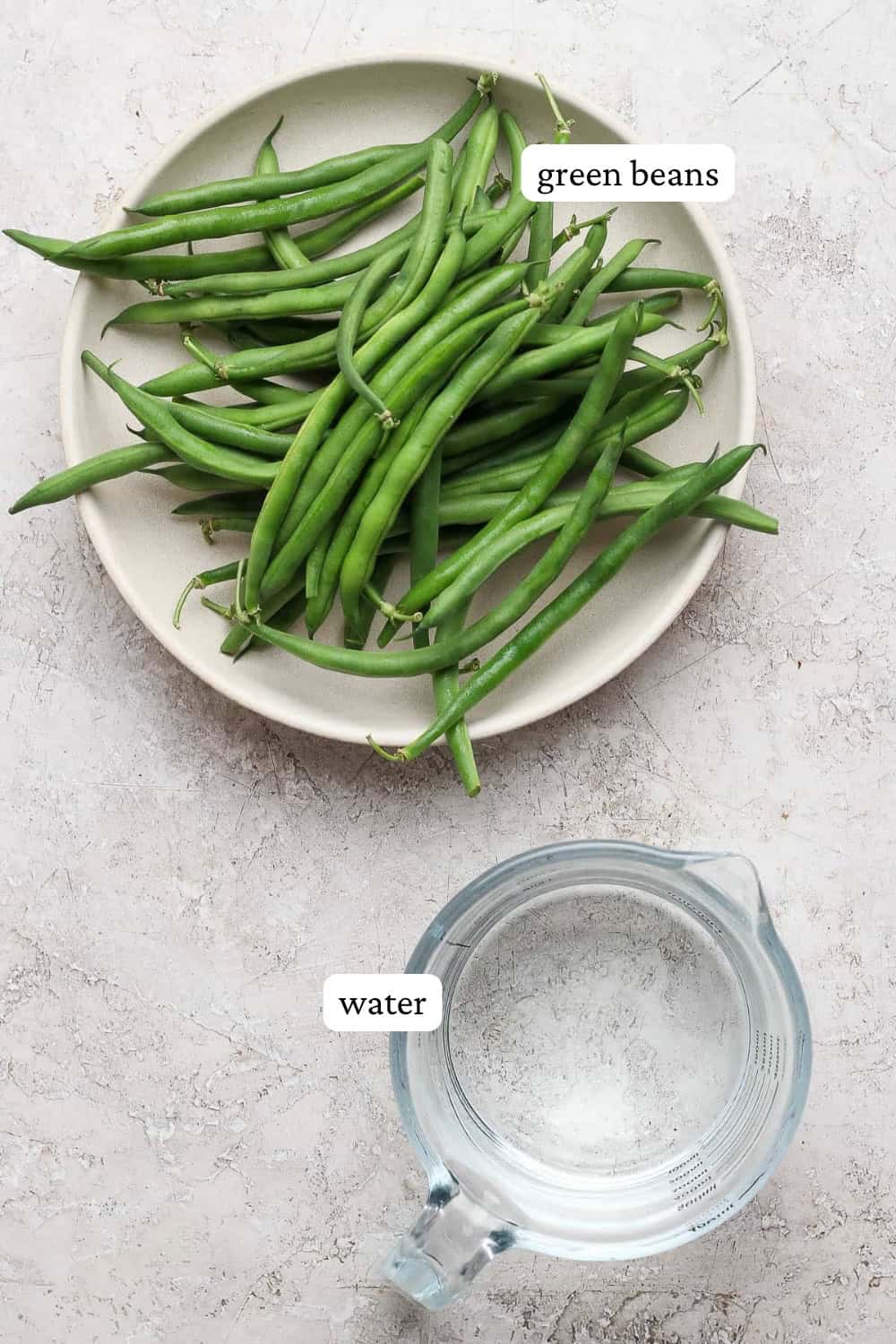 Ingredients for how to steam green beans in a bowl and measuring cup with labels.