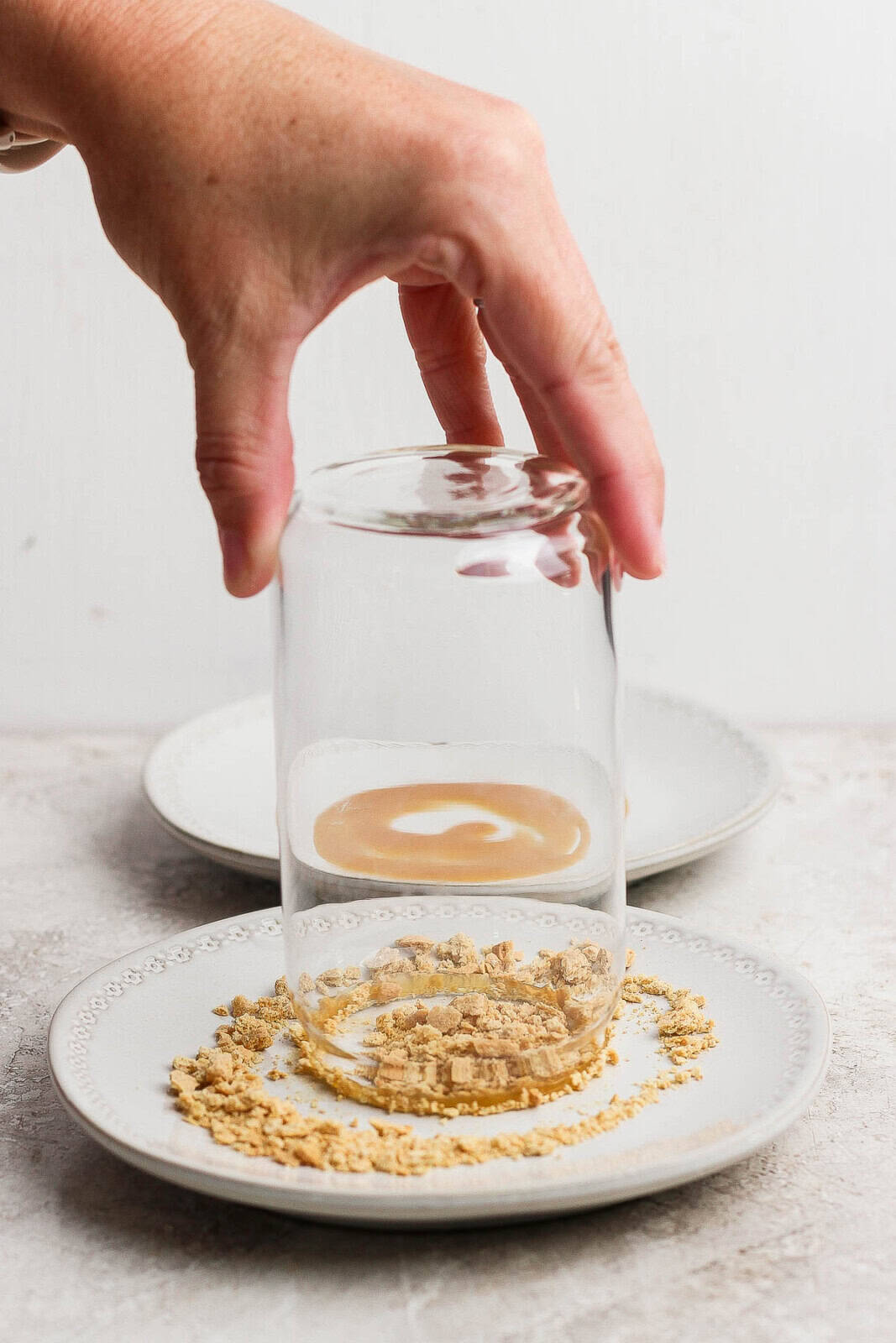 A tall glass for a pumpkin pie shake being twisted in crushed graham crackers.