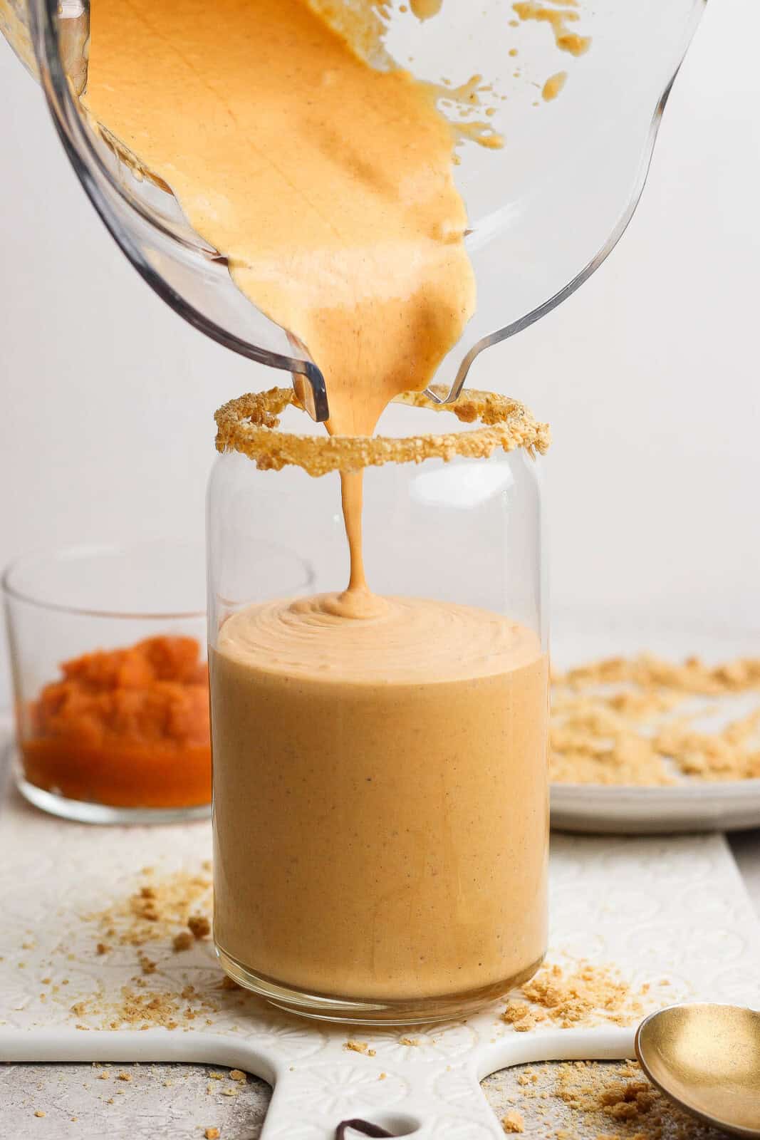 A pumpkin pie shake being poured into a glass with a graham cracker rim.