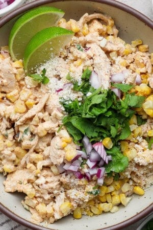 Street corn chicken salad in a large bowl with fresh cilantro and lime wedges.
