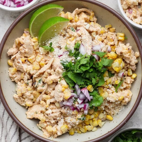 Street corn chicken salad in a large bowl with fresh cilantro and lime wedges.