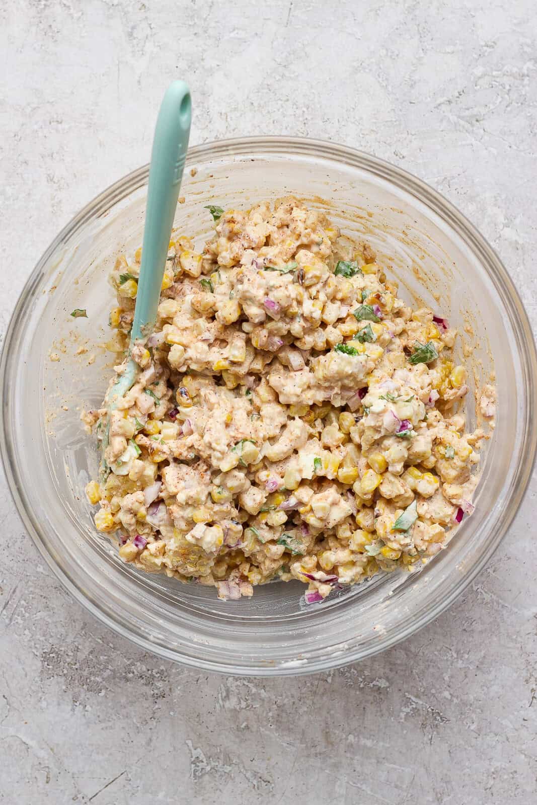 Mexican street corn mixture for street corn chicken salad mixed together in a glass bowl with a spatula sticking out the side.