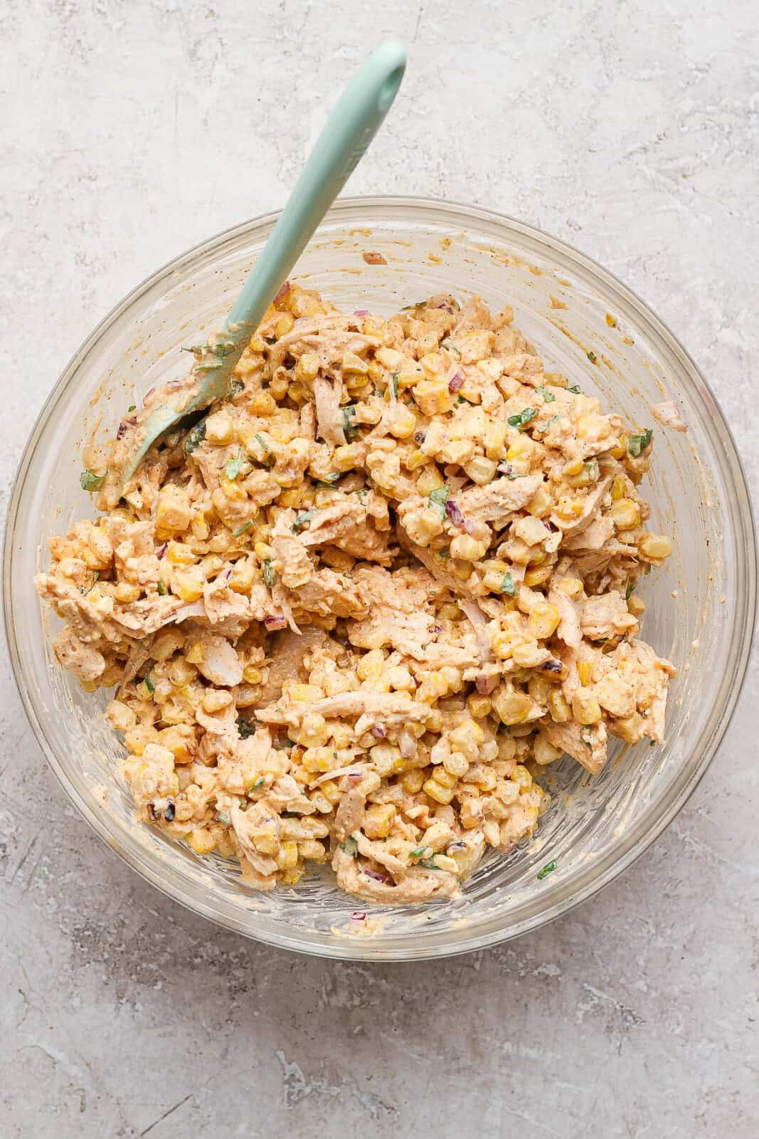 Street corn chicken salad fully mixed in a glass bowl with a spatula.