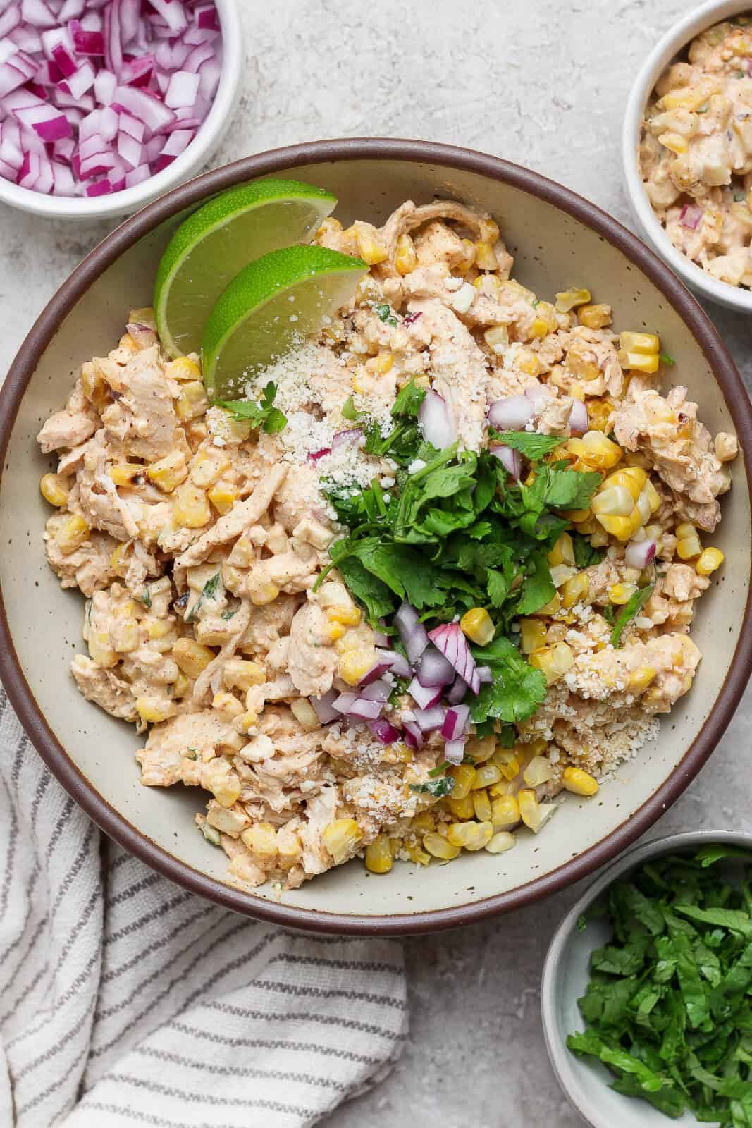 Street corn chicken salad in a serving bowl with cilantro, red onion, and lime wedges on top.