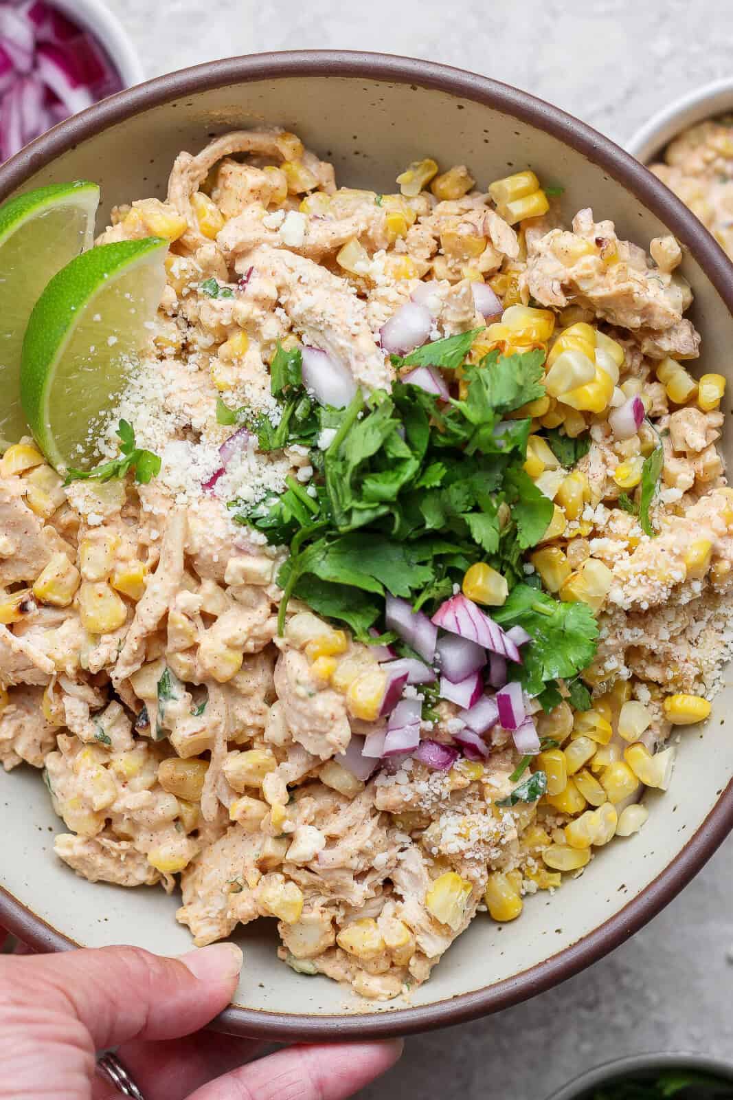 A large bowl of street corn chicken salad being held by a hand.