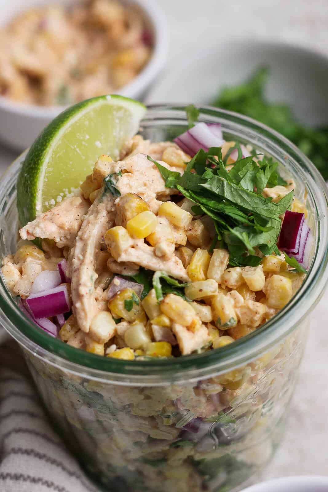 Street corn chicken salad in a tall glass jar with a lime wedge on top.