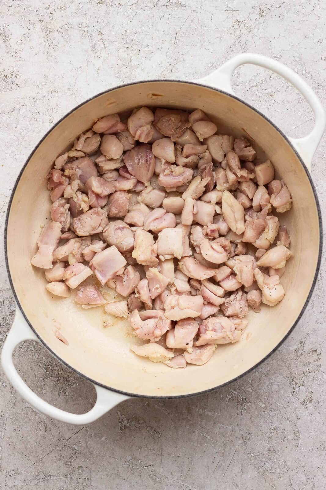 Cut-up pieces of chicken thighs searing in a dutch oven to make sweet potato chicken curry.