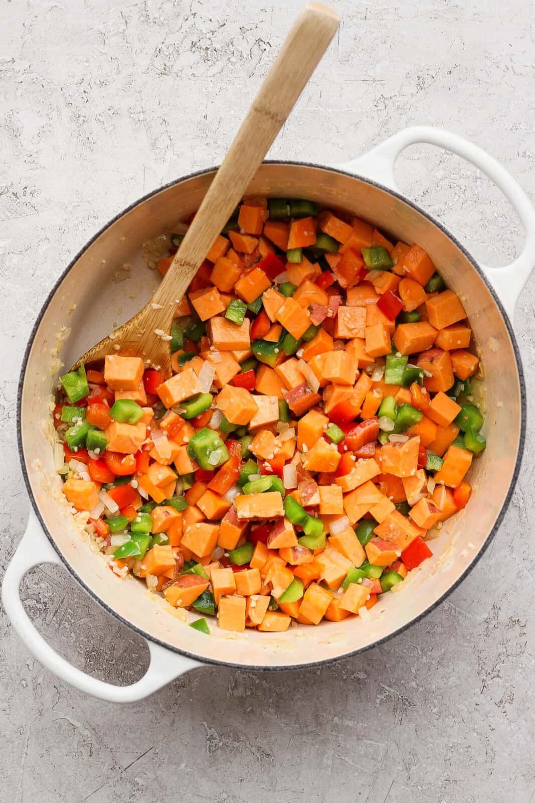 Onion, garlic, sweet potatoes, and bell peppers cooking in a dutch oven for sweet potato chicken curry.