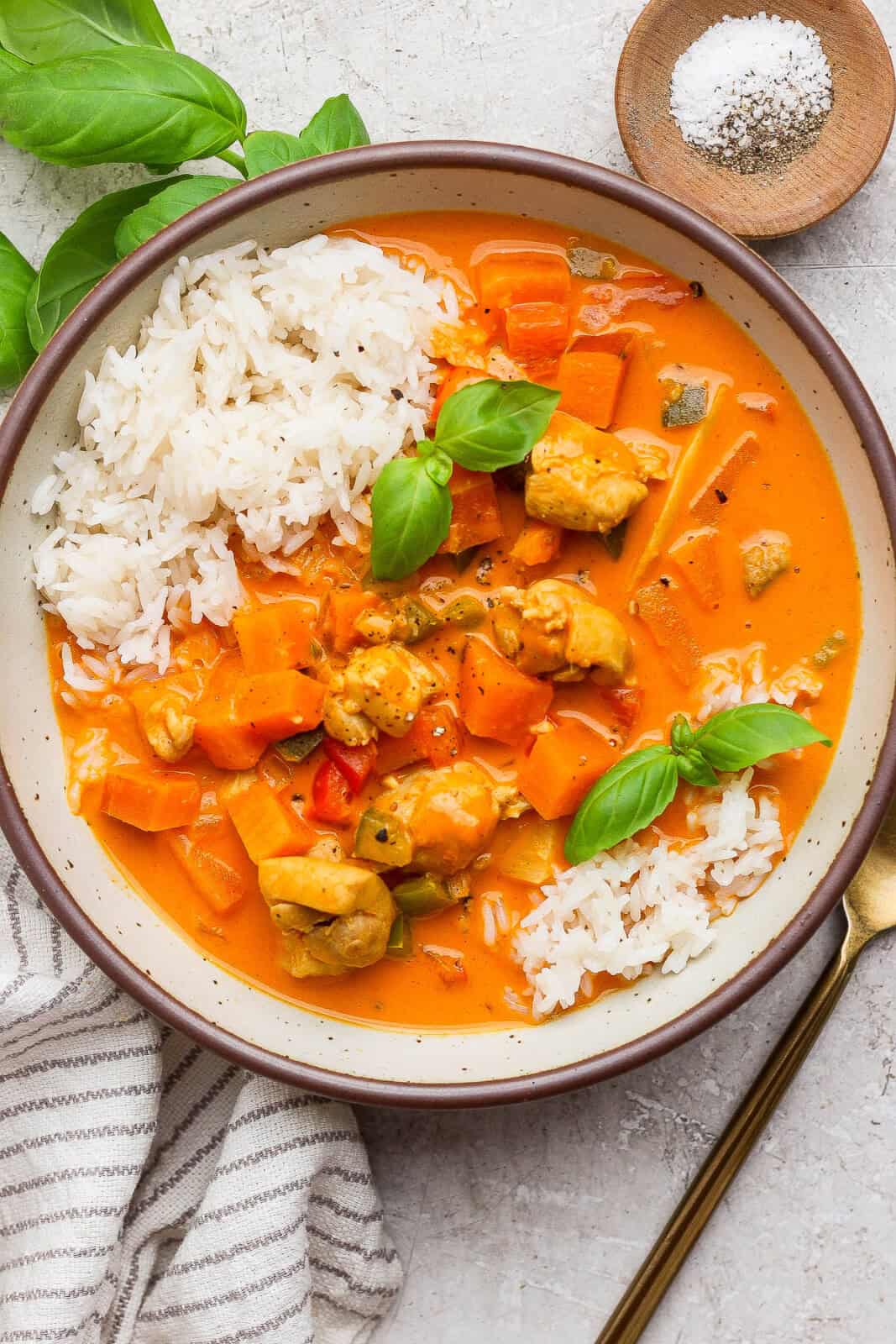 Sweet potato chicken curry in a bowl with white rice next to a gold fork and small dish of salt and pepper.