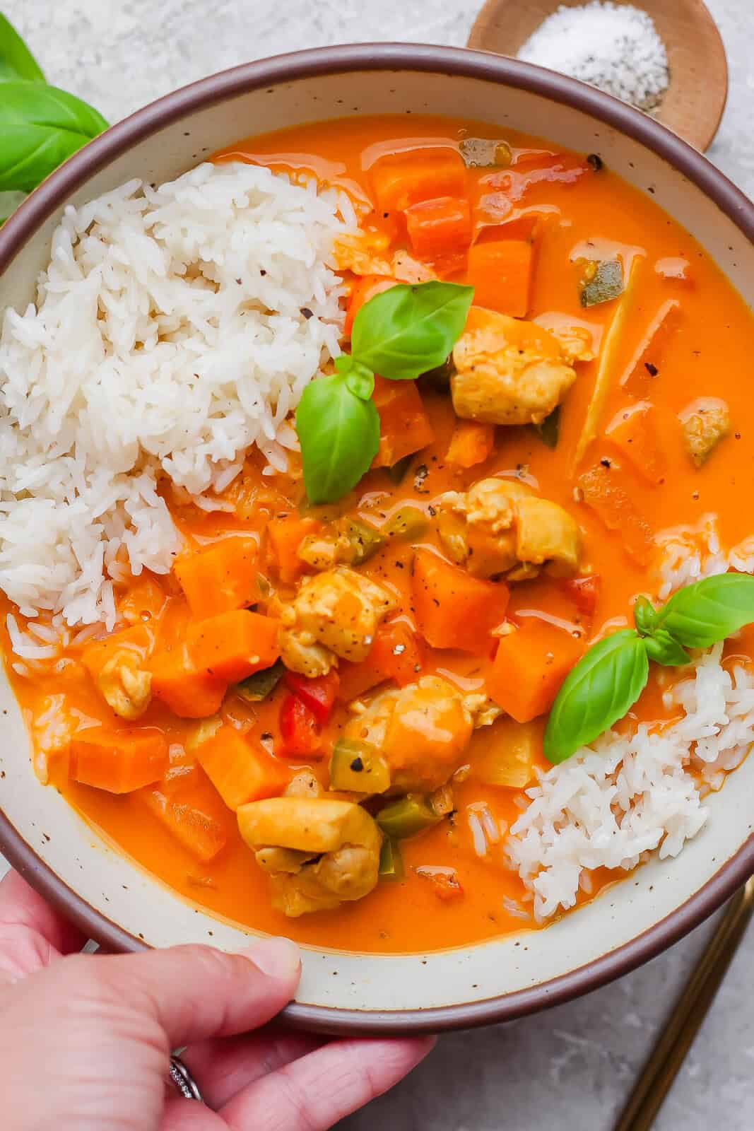 A bowl of sweet potato chicken curry served over rice with some fresh basil.