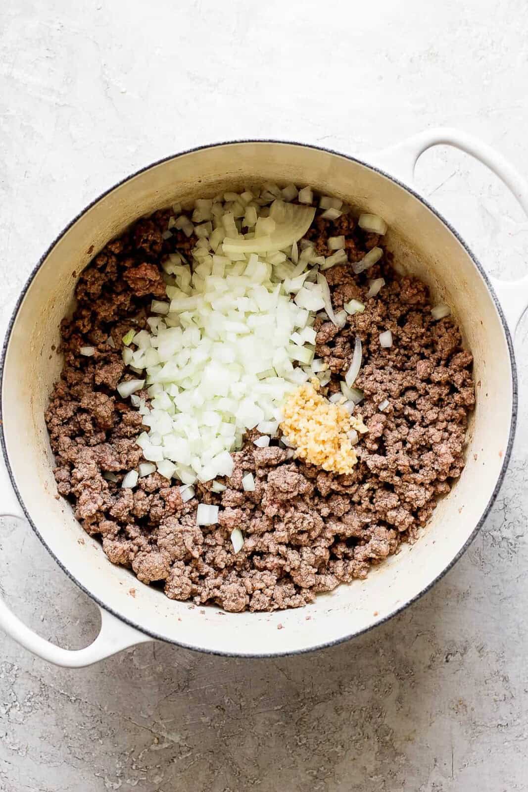 Diced onion and minced garlic added to a pot of ground beef for taco soup.