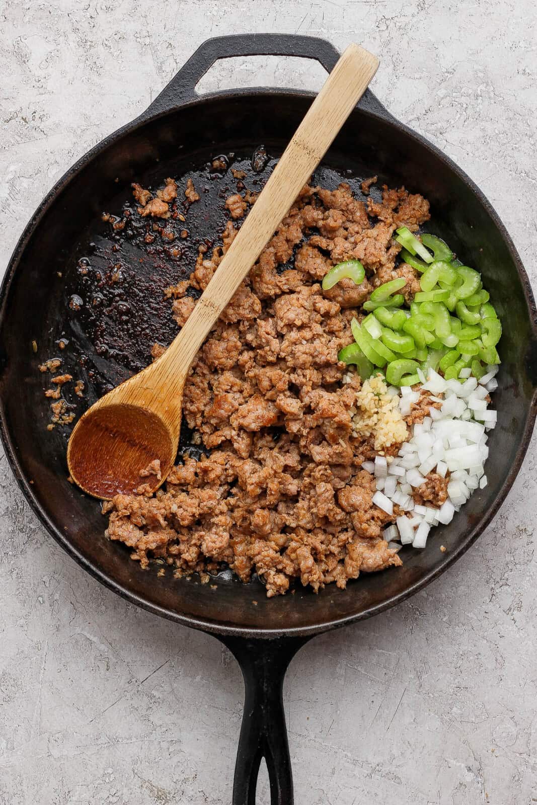 Browned sausage in a skillet with celery, onion, garlic and a wooden spoon to make sausage and apple stuffed acorn squash.