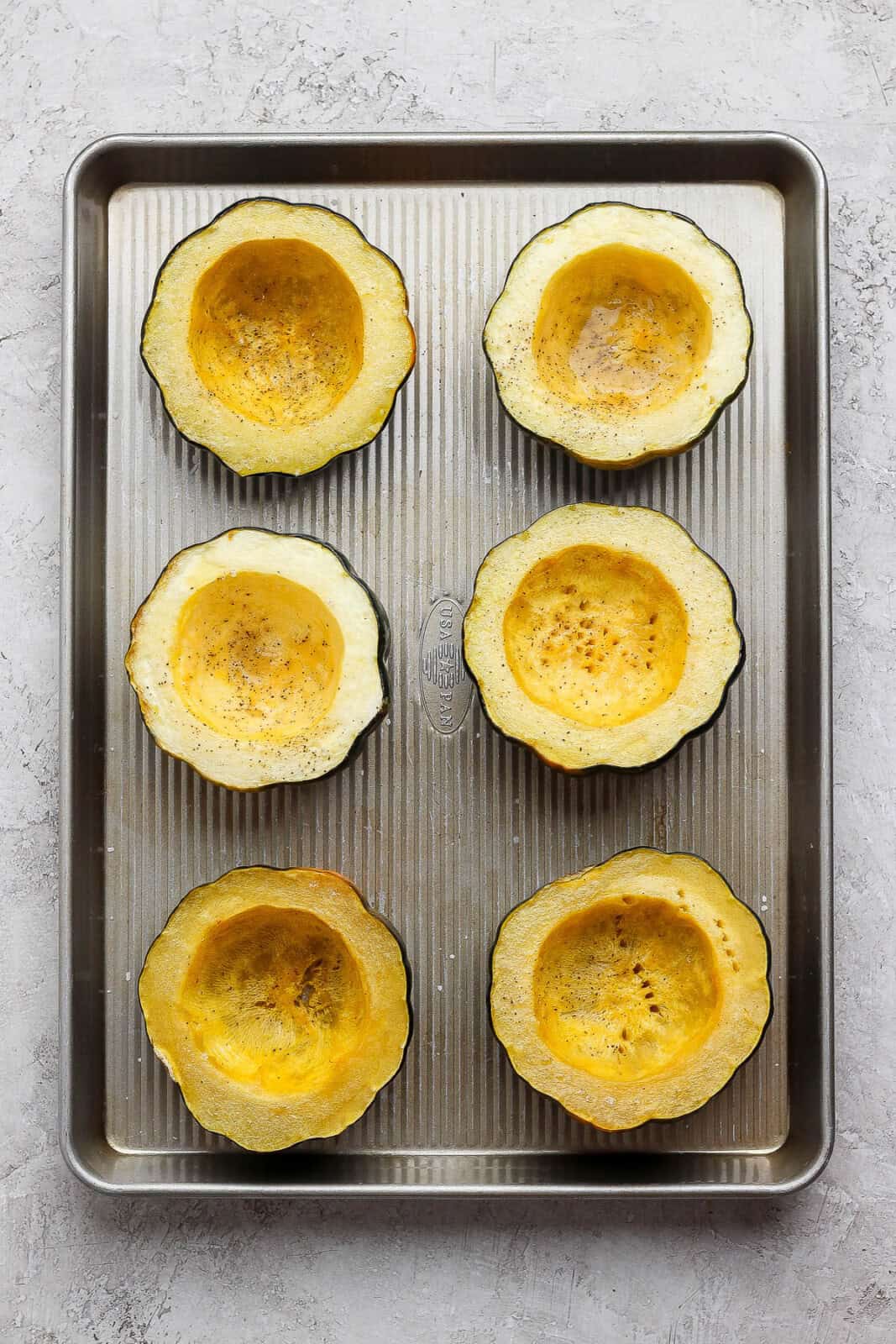 Roasted acorn squash halves on a sheet pan to make sausage and apple stuffed acorn squash.