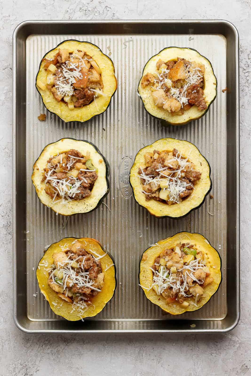 Six sausage and apple stuffed acorn squash halves before baking in the oven.