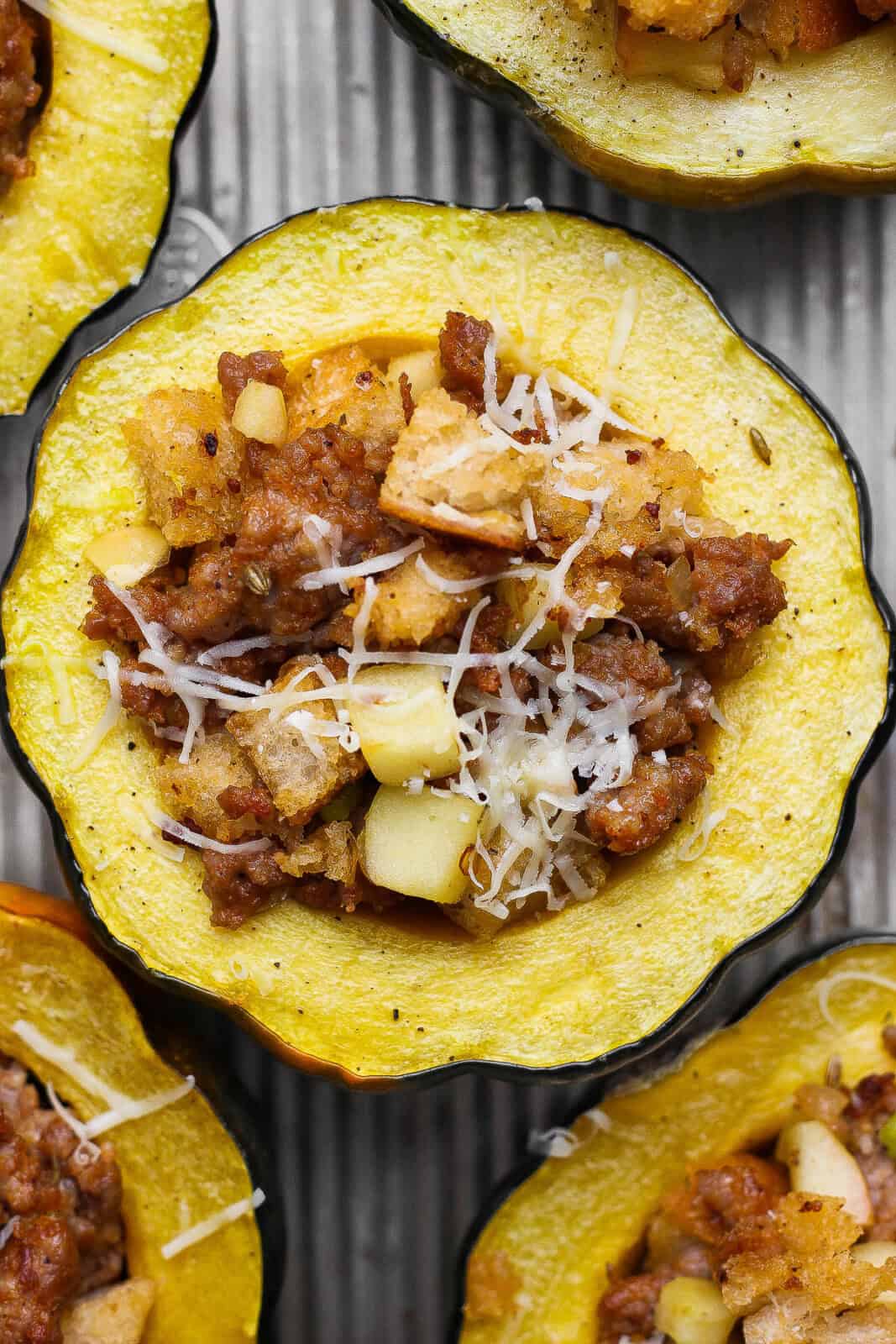 A baked sausage and apple stuffed acorn squash next to more stuffed squash on a sheet pan.