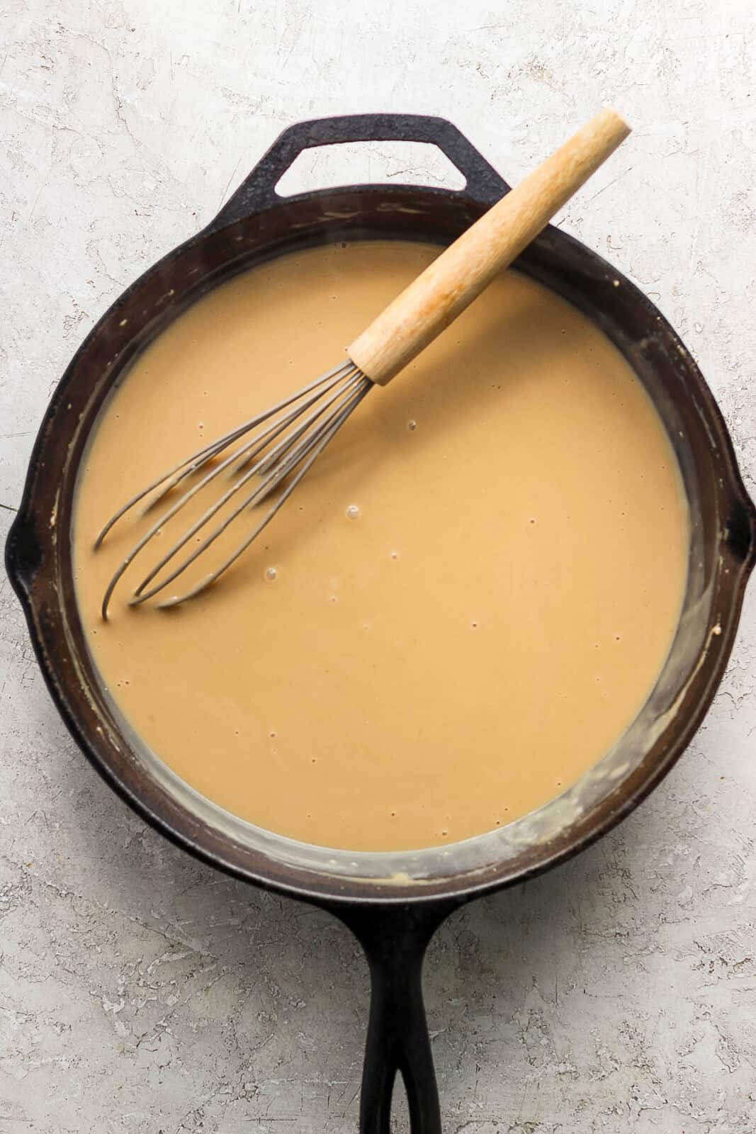 Swedish meatball gravy in a cast iron skillet with a whisk.