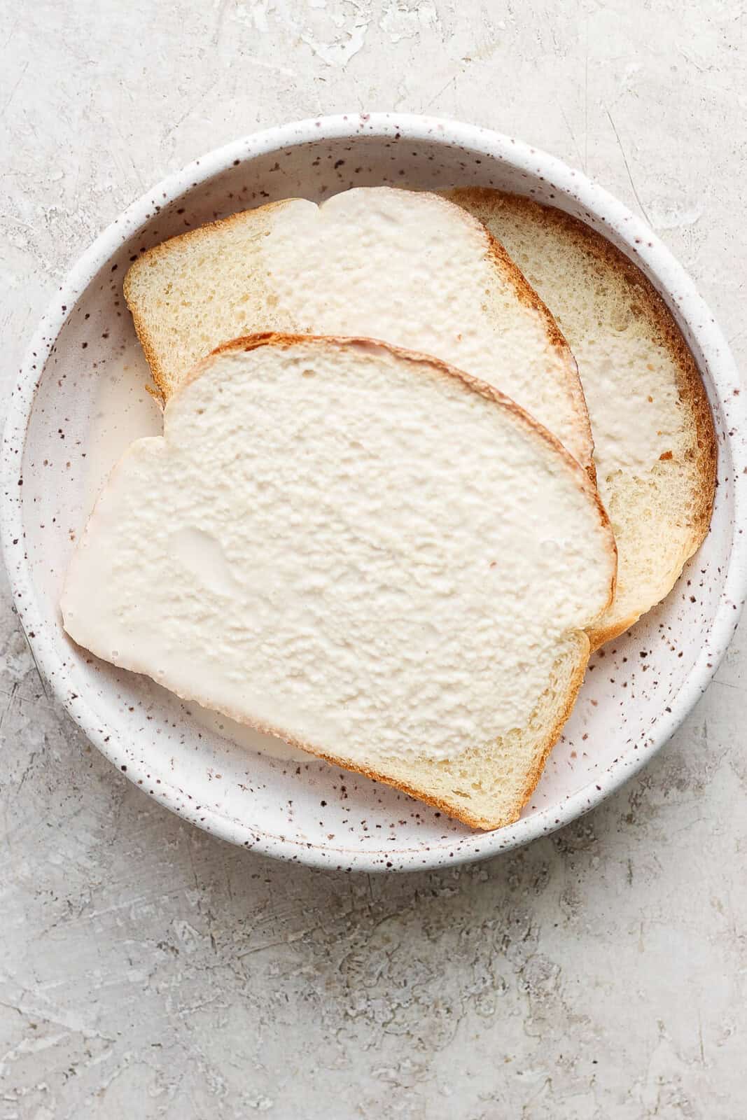 Three slices of bread soaking in dairy-free creamer for making Swedish meatballs.