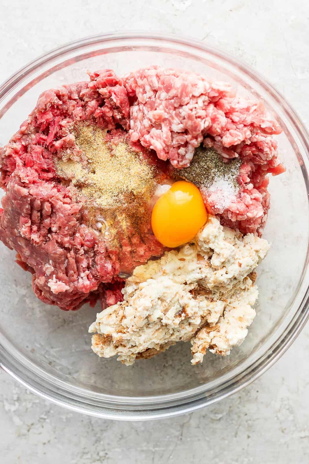 Swedish meatball ingredients in a glass bowl before being mixed to form meatballs.