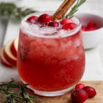 A cranberry kombucha mocktail in a glass with cranberries and a cinnamon stick.