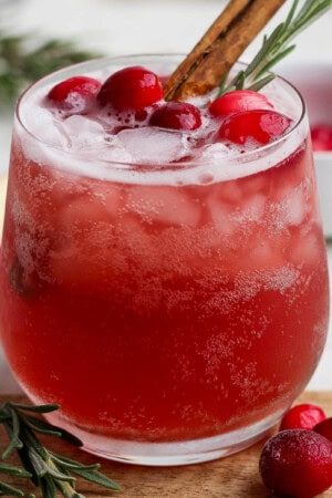 A cranberry kombucha mocktail in a glass with cranberries and a cinnamon stick.