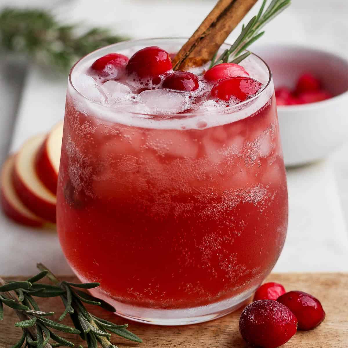 A cranberry kombucha mocktail in a glass with cranberries and a cinnamon stick.