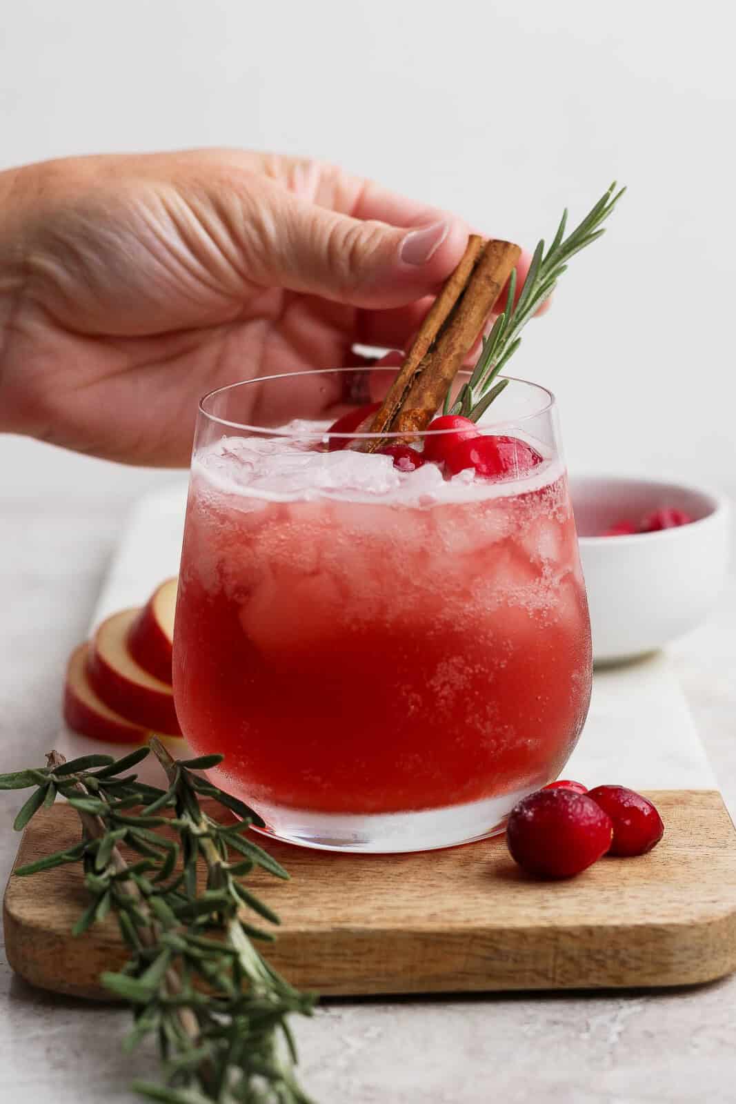 Someone placing a cinnamon stick in a cranberry kombucha mocktail.