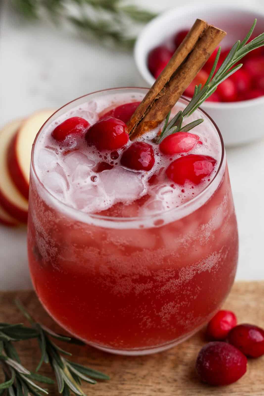 A glass of cranberry kombucha mocktail with cranberries, rosemary, and a cinnamon stick in the top.