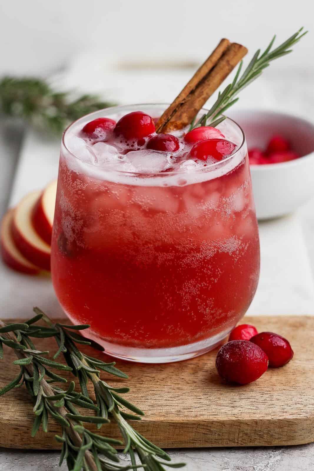 A cranberry kombucha mocktail with garnishes in the glass and next to the glass.