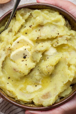 Horseradish mashed potatoes in a large bowl being held with 2 hands.