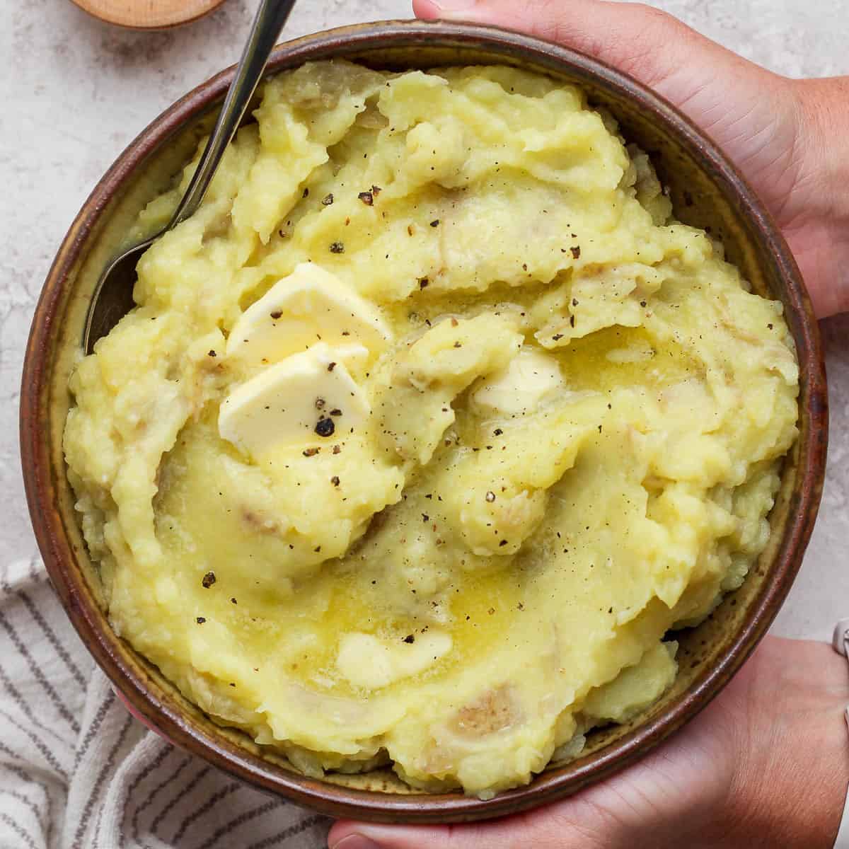 Horseradish mashed potatoes in a large bowl being held with 2 hands.