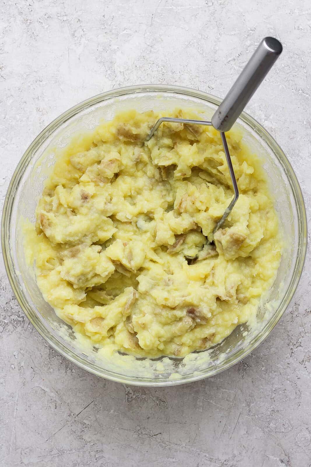 Horseradish mashed potatoes in a glass bowl with a manual hand masher.