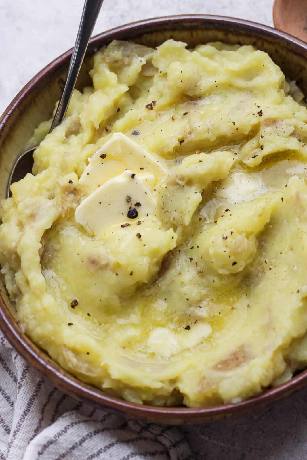 A bowl of horseradish mashed potatoes in a bowl with more butter and a spoon sticking out the side.