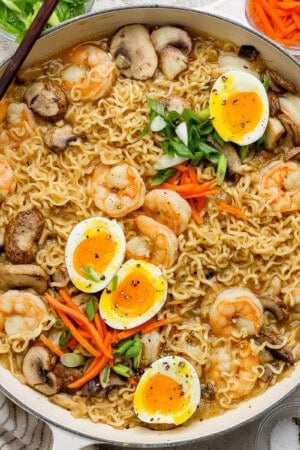 A braising pan full of shrimp ramen with soft boiled eggs cut in half on top.