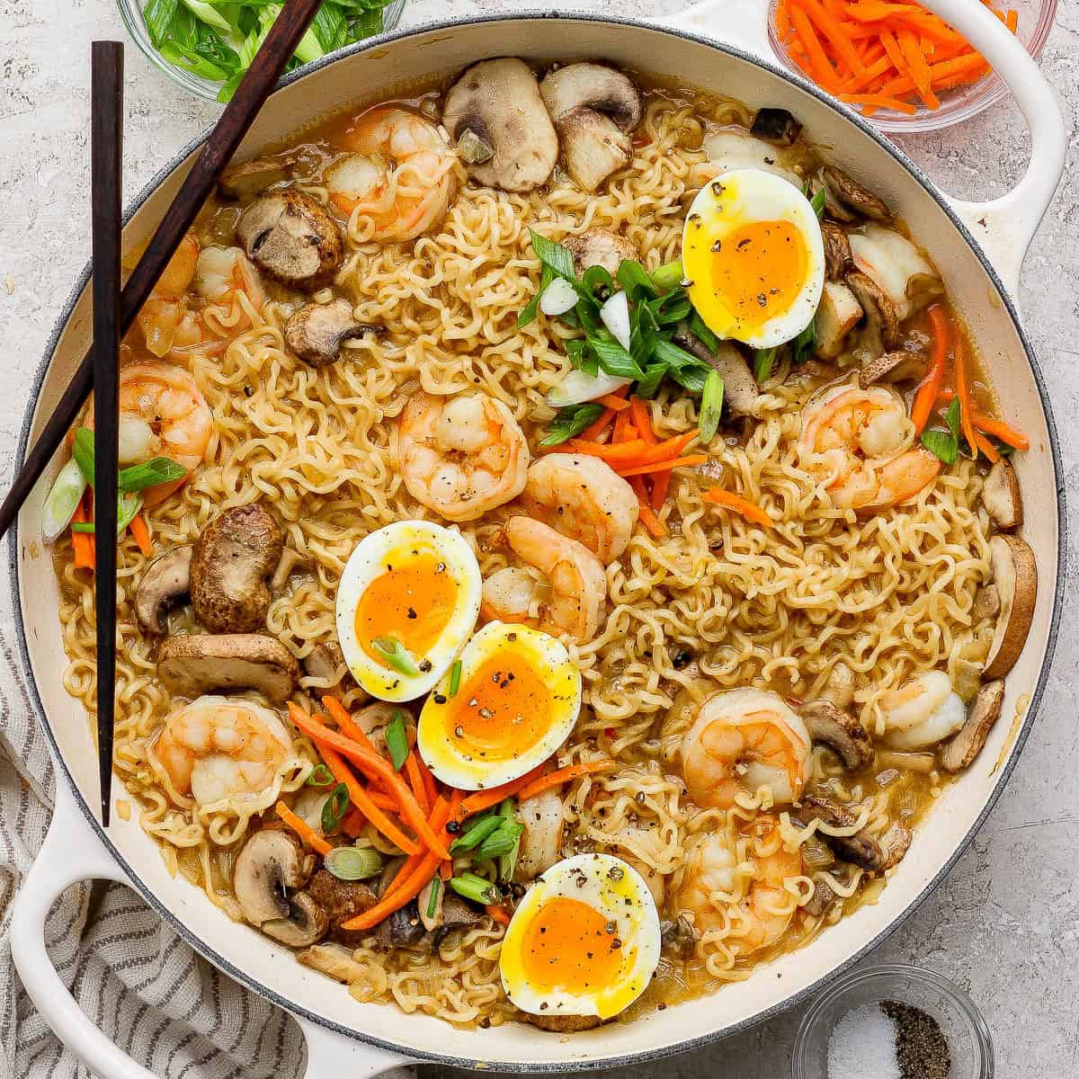 A braising pan full of shrimp ramen with soft boiled eggs cut in half on top.