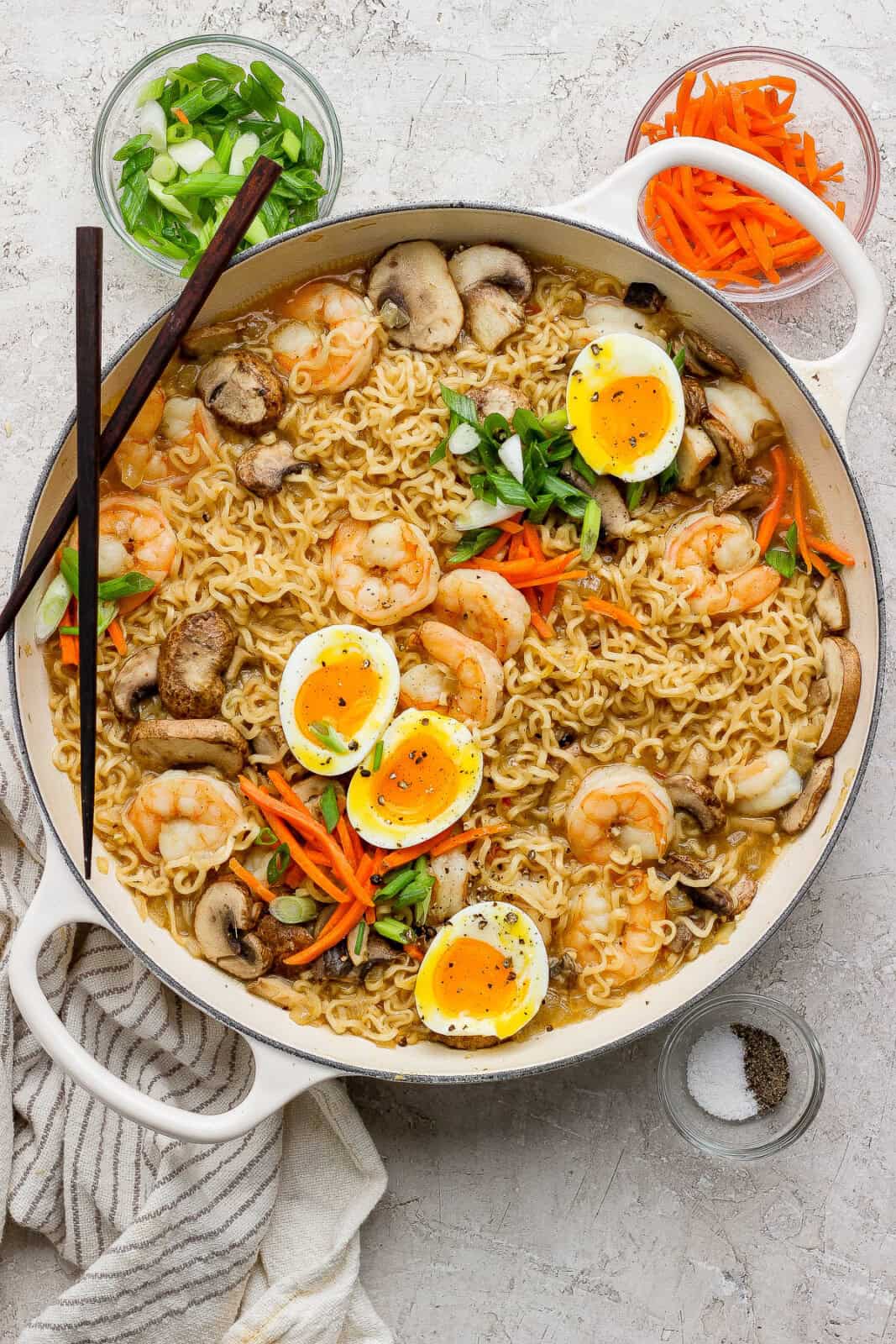 Shrimp ramen noodles in a large braiser pan with soft boiled eggs, matchstix carrots, and green onions on top.