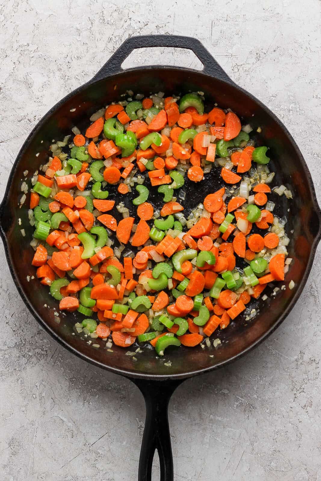 Garlic, onion, celery, and carrots sautéd in a cast iron skillet to make slow cooker chicken tortellini soup.