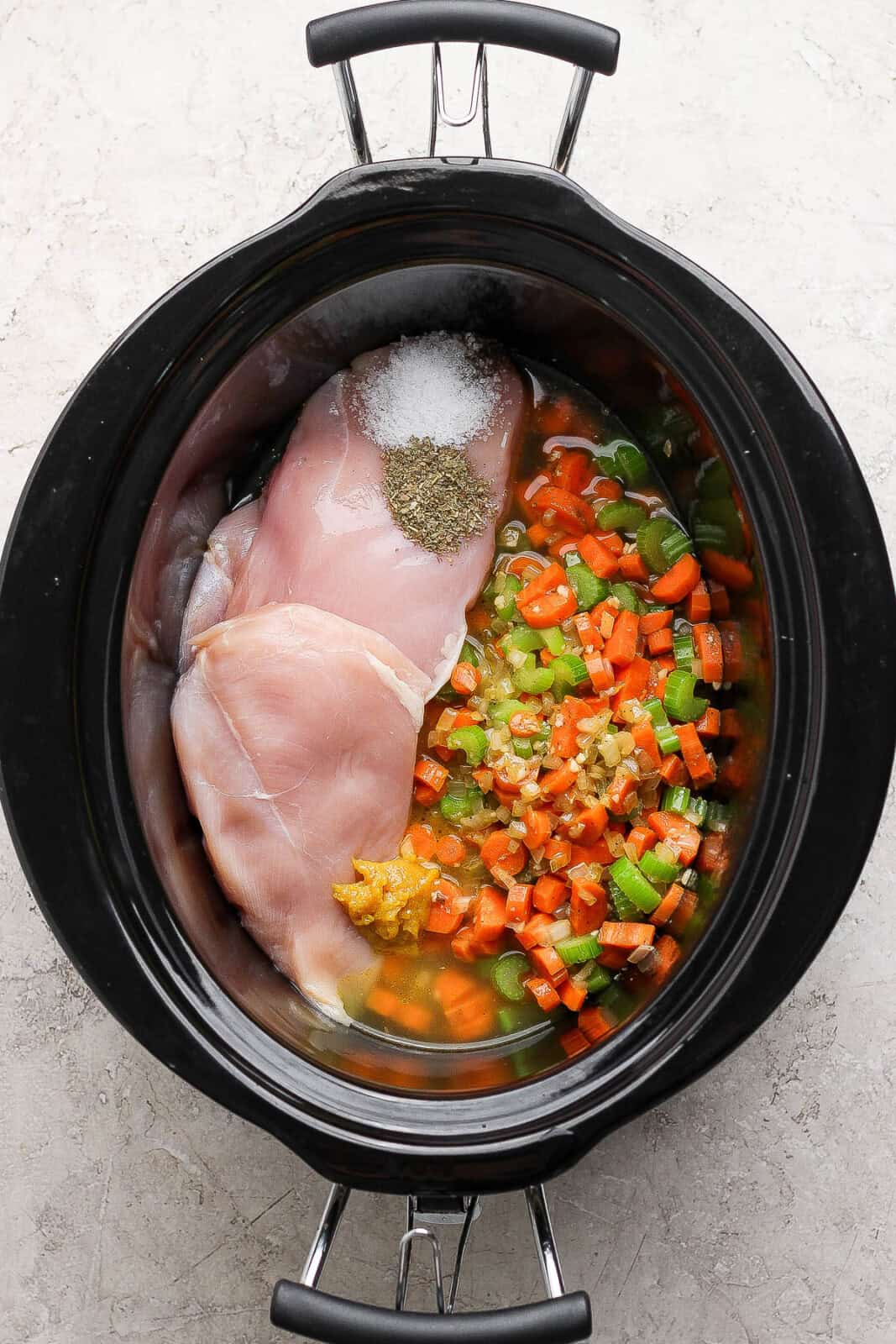 All of the slow cooker chicken tortellini soup ingredients in a slow cooker except for the cheese tortellini and spinach.