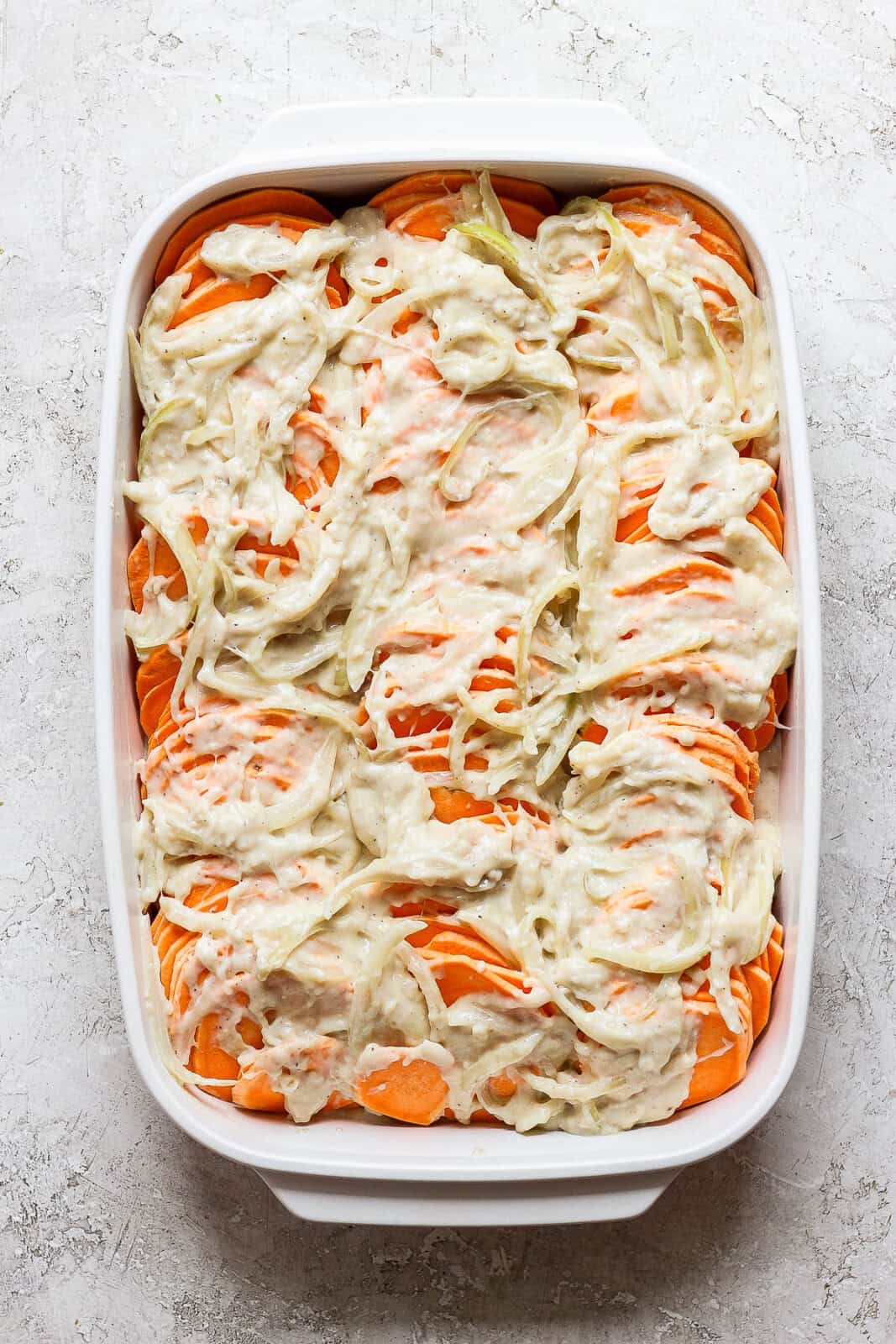 More cheesy sauce added on top of sliced sweet potatoes for sweet potato au gratin.
