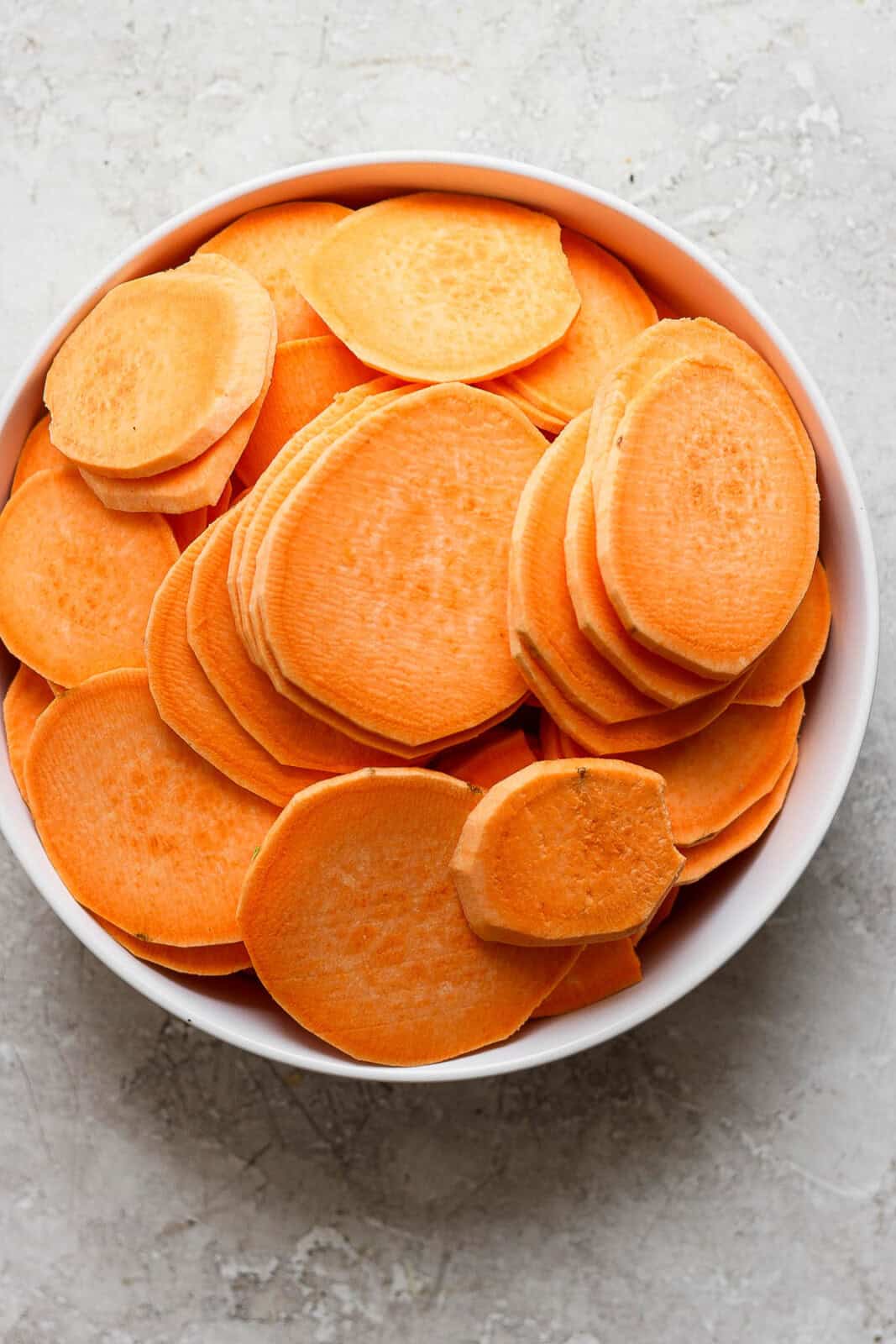 Sliced sweet potatoes in a white bowl to make sweet potato au gratin.