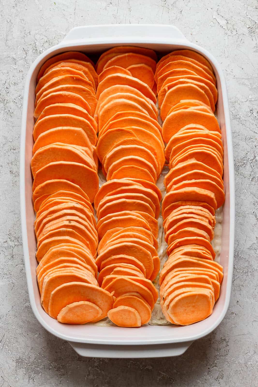 Sliced sweet potatoes added to the baking pan for sweet potato au gratin.