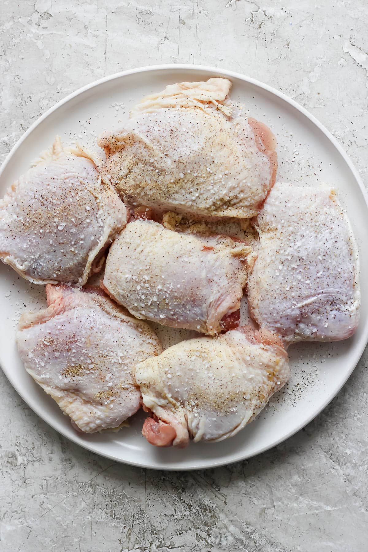 Six bone-in, skin-on chicken thighs on a plate to make ginger turmeric chicken soup with orzo.