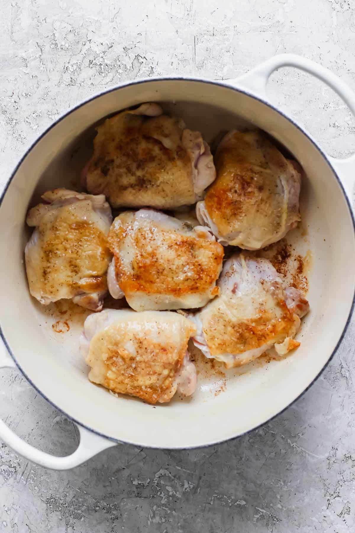 Six seared bone-in, skin-on chicken thighs in a soup pan to make ginger turmeric chicken soup.