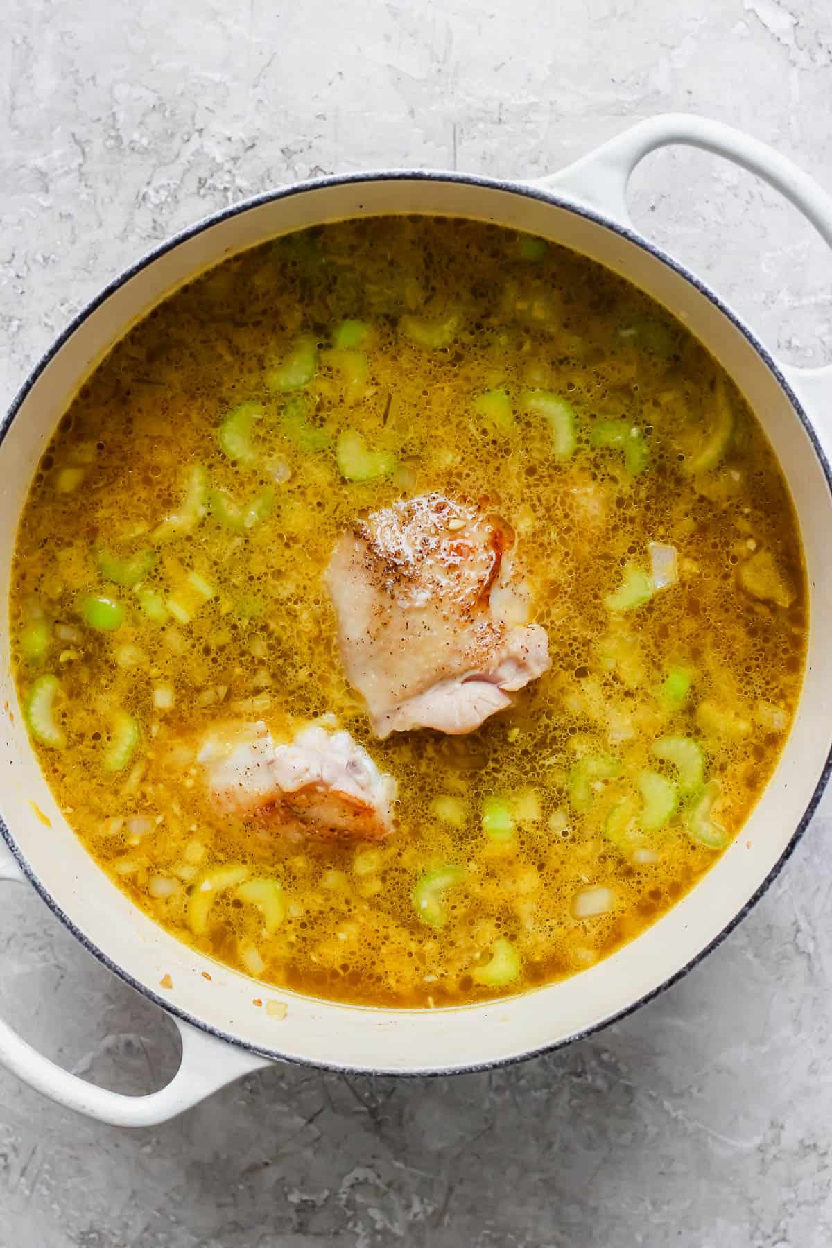 Ginger turmeric chicken soup with uncooked chicken in a dutch oven.