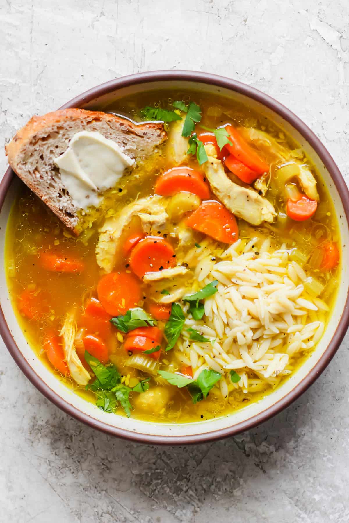 Ginger turmeric chicken soup with orzo in a bowl with buttered bread.
